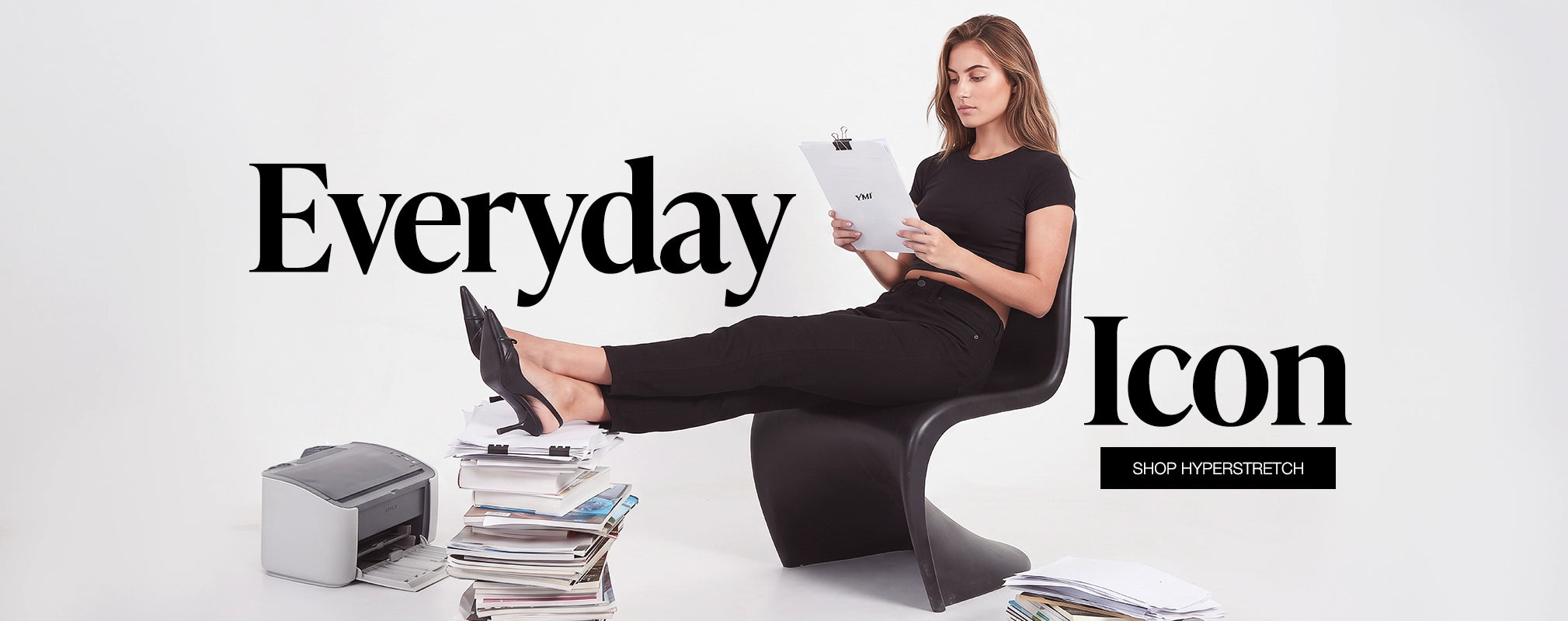 A woman in a black outfit sits in a black sculptural chair, reading a magazine, with her foot resting on a printer. Large text reads 'Everyday Icon' and 'SHOP HYPERSTRETCH' on a white studio background.