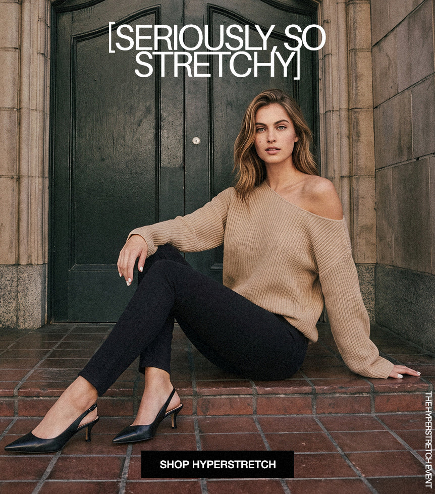 A woman sits on brick steps in front of a dark wooden door, wearing a beige off-the-shoulder ribbed sweater, black leggings, and black pointed mule heels. Large text at the top reads '[SERIOUSLY, SO STRETCHY]' and a black banner at the bottom says 'SHOP HYPERSTRETCH'.