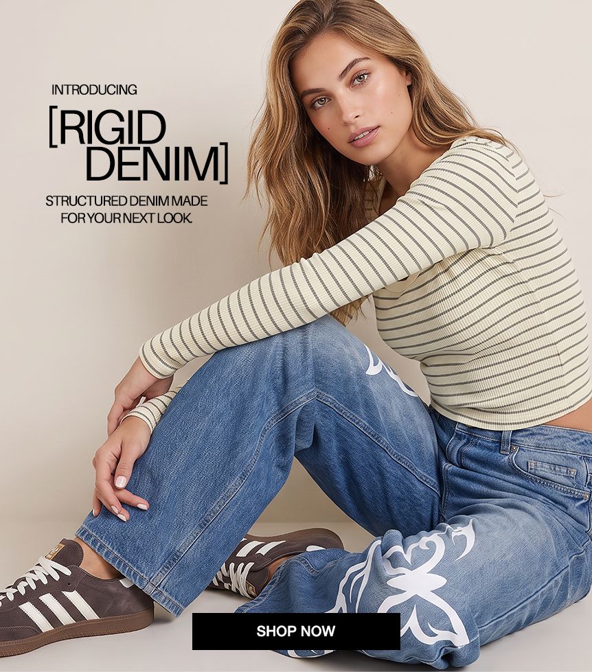 A woman models a beige and navy striped long-sleeve top paired with blue jeans featuring white graphic prints and brown sneakers, set against a light beige background with overlay text for 'Rigid Denim'.