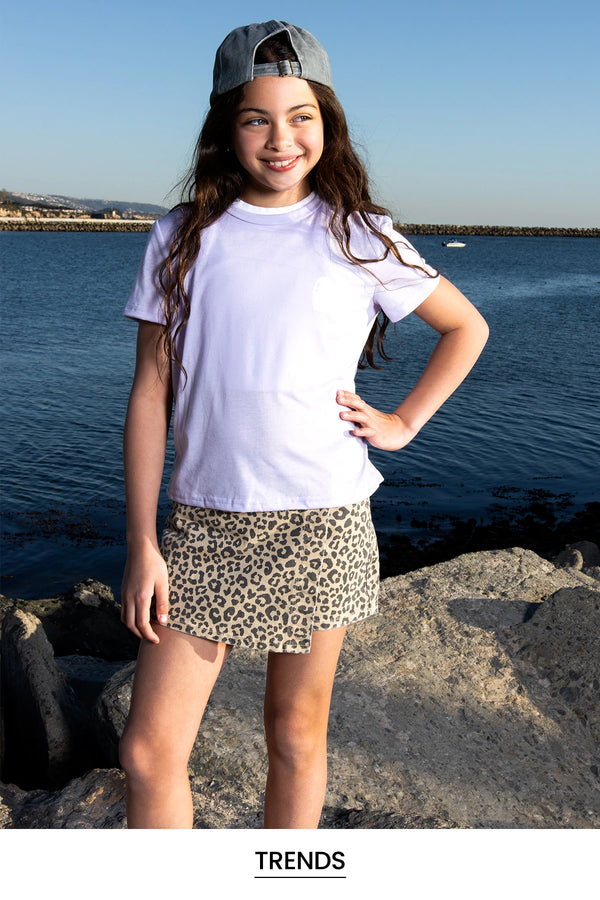 Girl standing by a body of water wearing a white t-shirt and leopard print skirt.